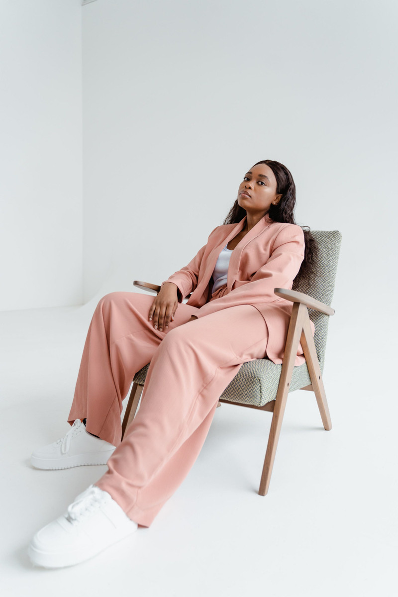 A rose relaxed suit, seated in a studio chair.